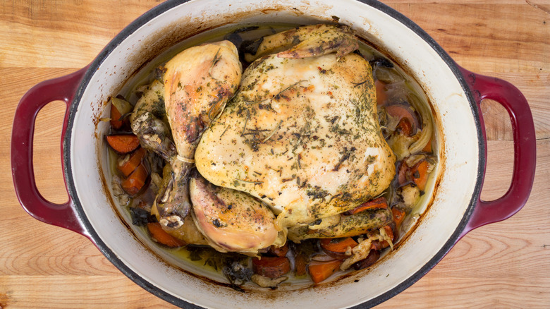 Chicken pot roast in red slow cooker on wood surface.