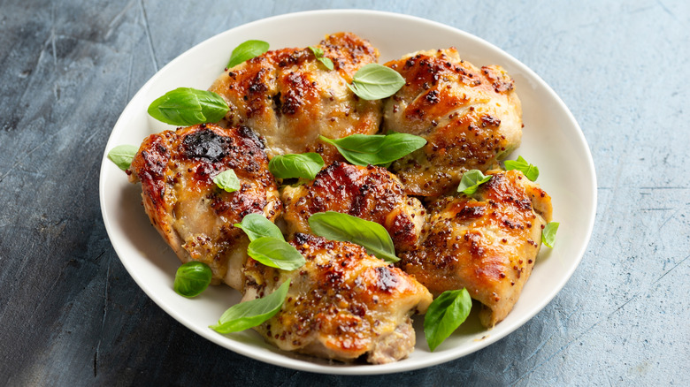 Honey mustard chicken thighs on white plate with fresh herbs on top.