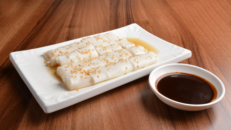 Cheong fan accompanied by soy sauce in a side bowl.