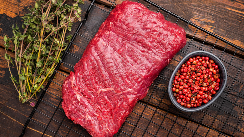 An uncooked flank steak is arranged with herbs and spices.