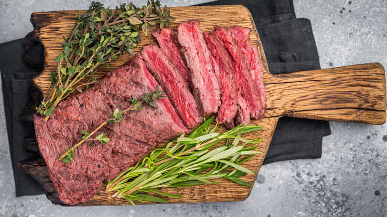 A flank steak has been sliced on a cutting board to reveal a rosy rare interior.