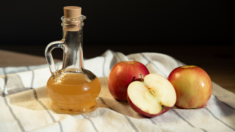 Apple cider vinegar in a glass bottle next to apples on a dishcloth