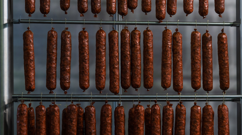 Bologna logs hanging from thin metal bars in a smokehouse