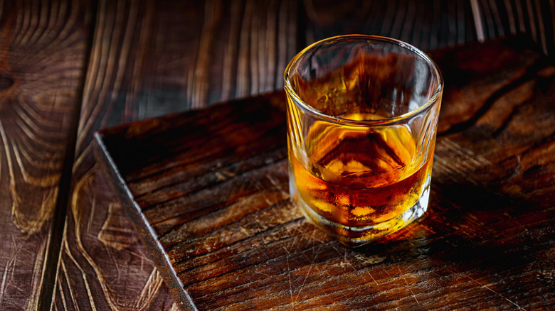 A glass of bourbon sitting on a scratched-up wooden tray