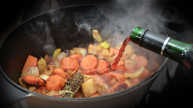 Red wine being poured into a pot of cooking vegetables