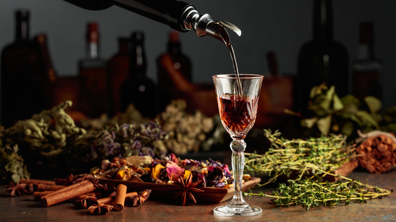 Brown liquid being poured into a glass against a backdrop of botanicals