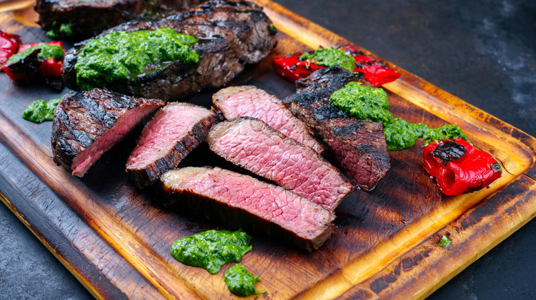 A sliced picanha steak with chimichurri sauce and chiles on a cutting board