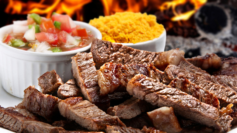 Sliced, grilled picanha steak on a plate with sides of farofa and salsa vinaigrette