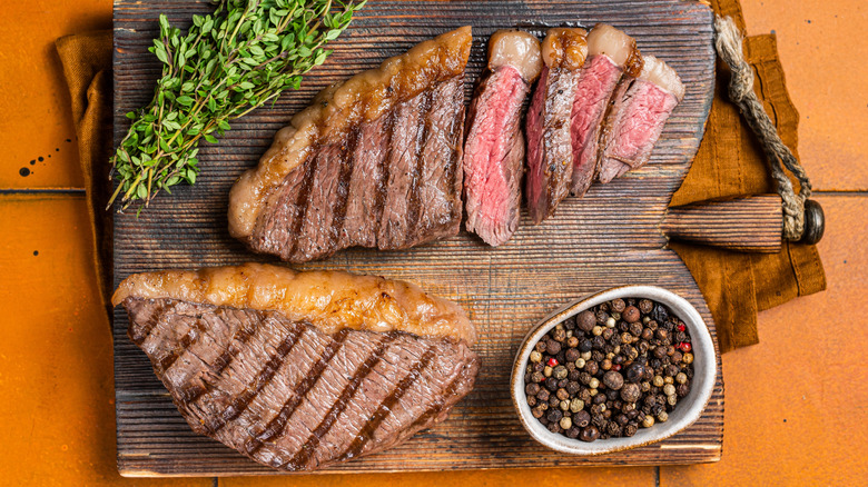 Two grilled picanha steaks on a cutting board with peppercorns and thyme