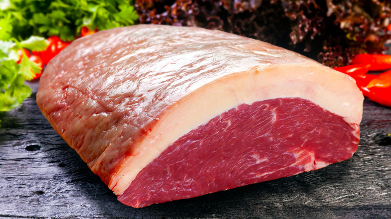 A raw picanha steak before being sliced on a cutting board
