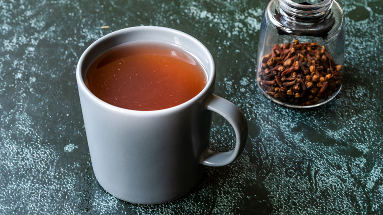 Sumac tea in white mug next to bottle of cloves