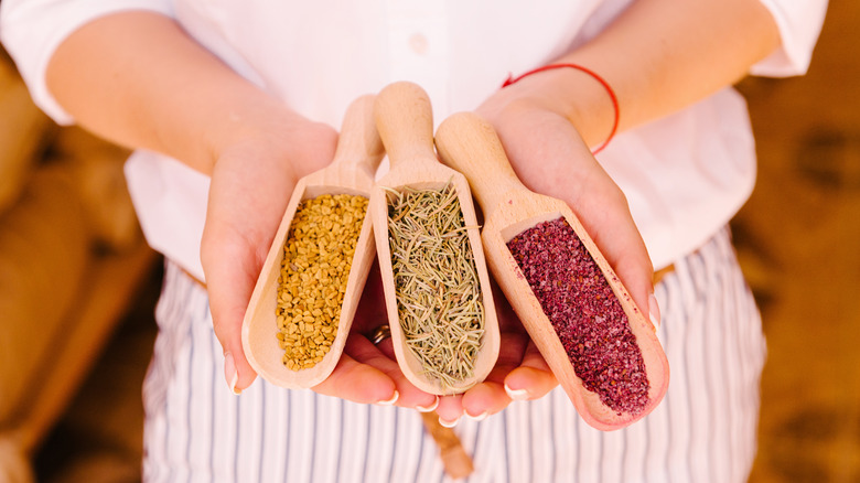 Woman's hands holding three wooden scoops filled with spices including ground sumac