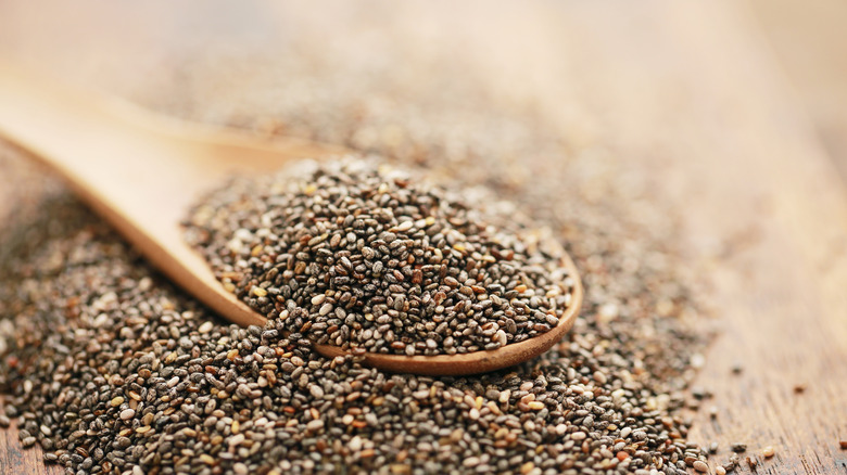 A spoonful of chia seeds set against a blurry, rustic background.