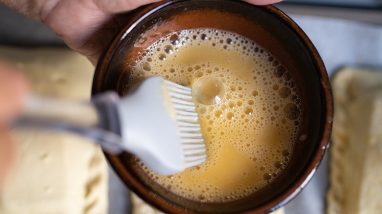 Dipping a silicon spatula into a frothy egg wash.