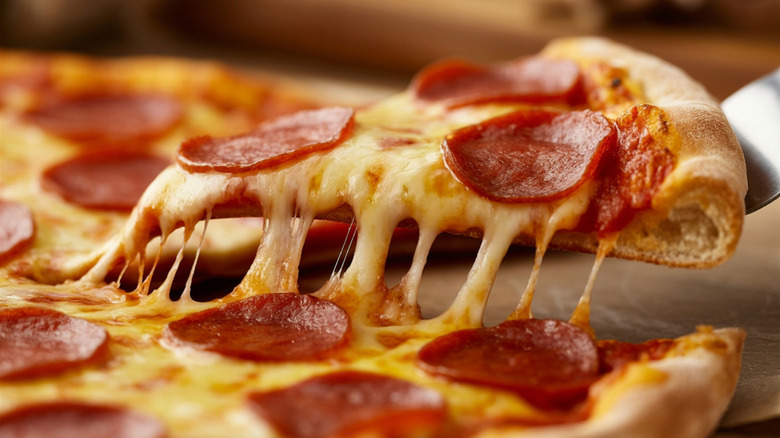 A pepperoni pizza slice being taken from a whole pie