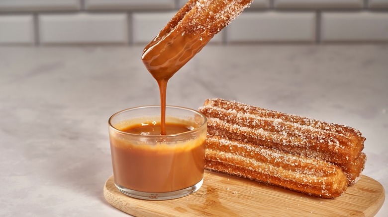 Churro being dipped in dulce de leche