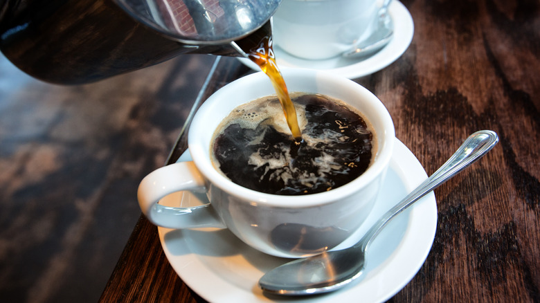 Coffee being poured into white cup with spoon