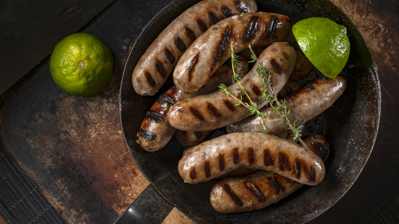 Grilled Italian sausages in a skillet with limes