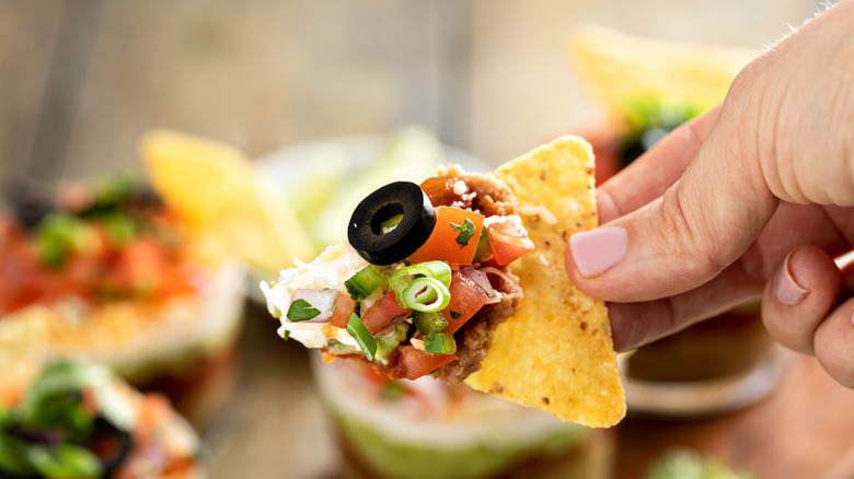 A tortilla chip covered in many different ingredients, like tomatoes, black olives, and green onions