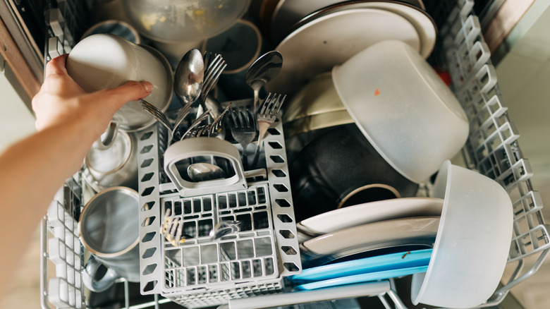 Hand placing a cup into a full dishwasher