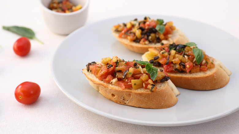 A plate of bruschetta topped with vegetables and basil.