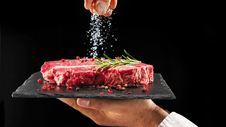 A hand salting raw steak