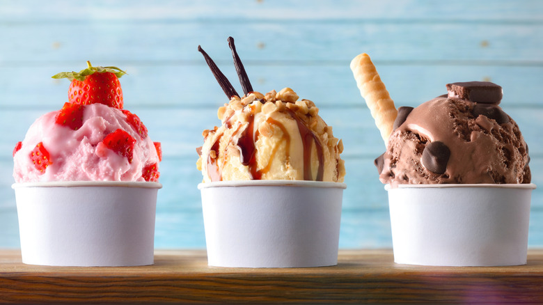 Three containers filled with different flavors of ice cream and various toppings