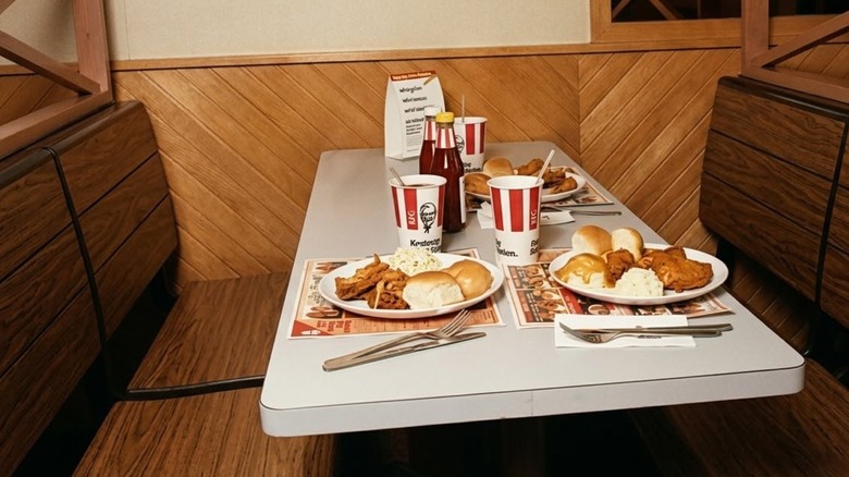 Table in a KFC booth set with plates of fried chicken, rolls, coleslaw, and mashedpotatoes