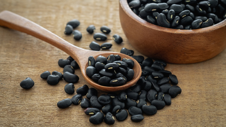 A bowl of black beans with a wooden spoon next to it.