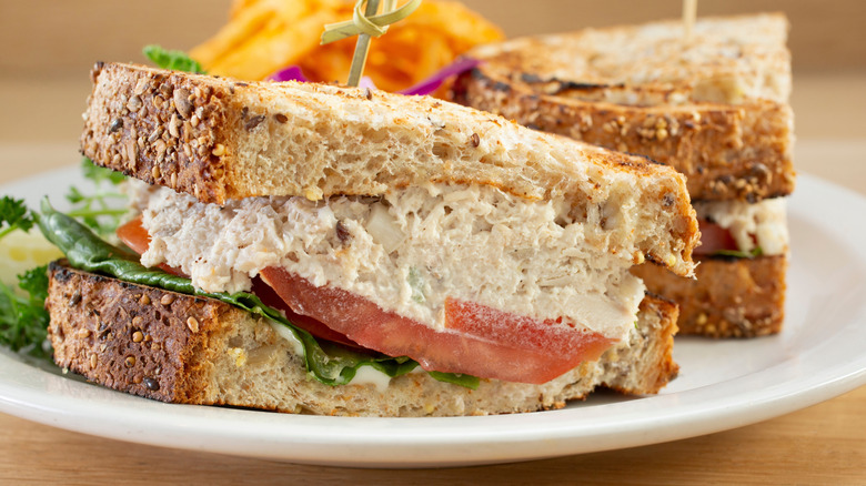 Tuna salad sandwich on rustic bread, with lettuce and tomato, sliced in half