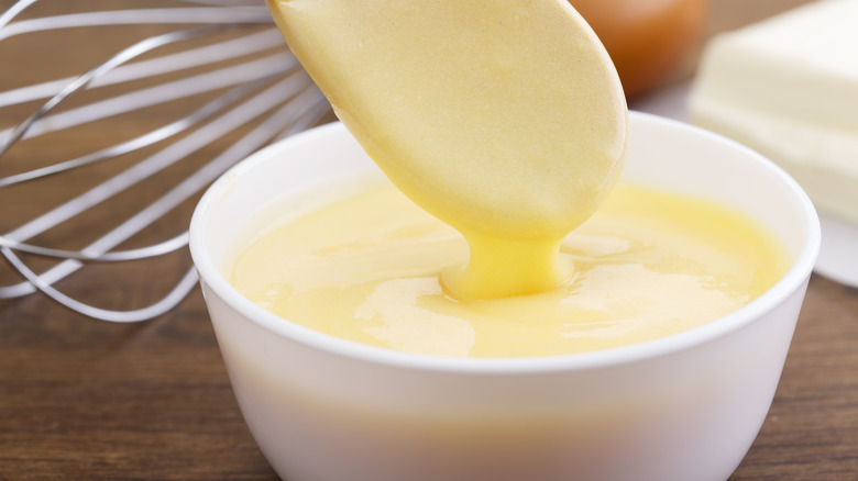 Spoon dipping into white bowl of hollandaise sauce.