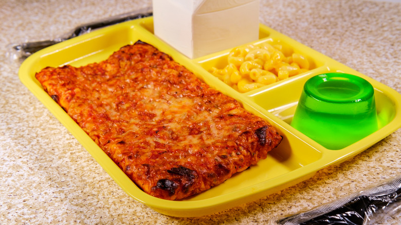an old-school cafeteria tray with slice of pizza, green Jell-O, and mac and cheese