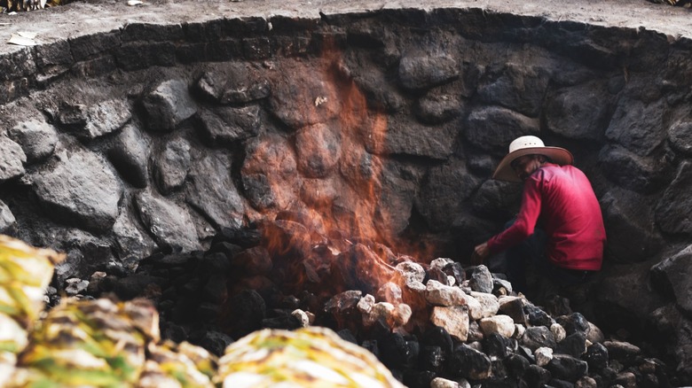 A worker roasting pina in a traditional mezcal brick over