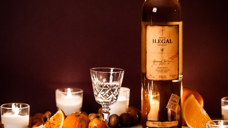 A bottle of Ilegal Mezcal with a glass, candles, and citrus