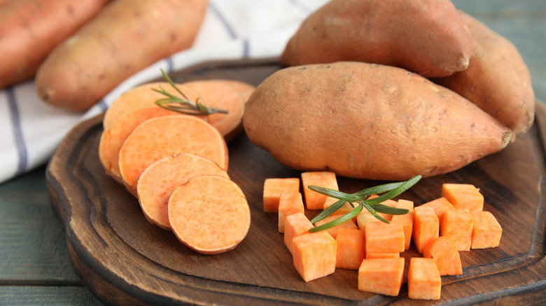 Wooden board with cut and whole sweet potatoes on table.