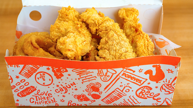 Popeyes box with three crispy chicken tenders on a bed of onion rings.