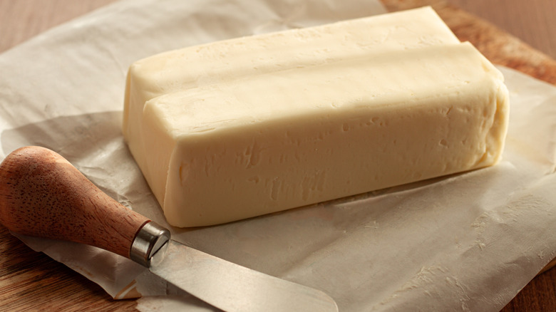 A large stick of butter sitting on its wrapper, a butter knife below.