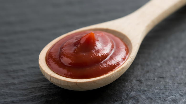 Thick ketchup in wooden spoon on a black table.