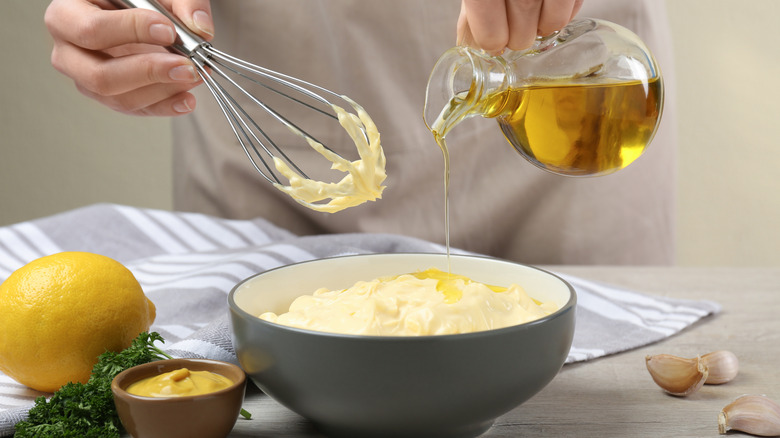 Person making homemade mayonnaise in ceramic bowl at wooden table