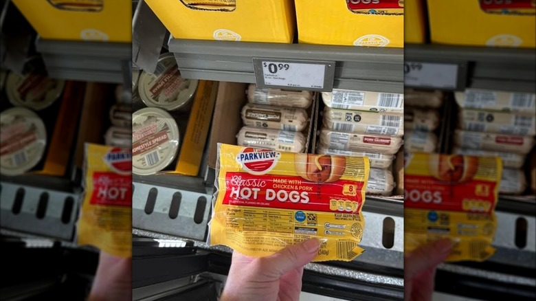 A hand holding a package of Parkview Classic hot dogs at Aldi in front of a 99-cent sign