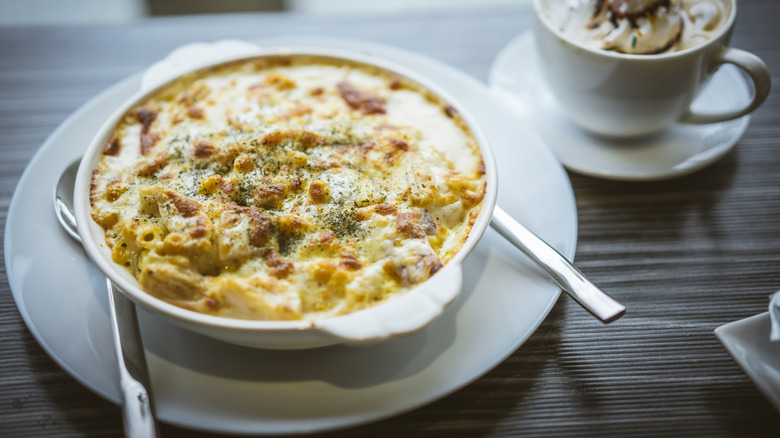 A dish of creamy, roasted mac and cheese fresh from th eoven on a white plate with silverware.