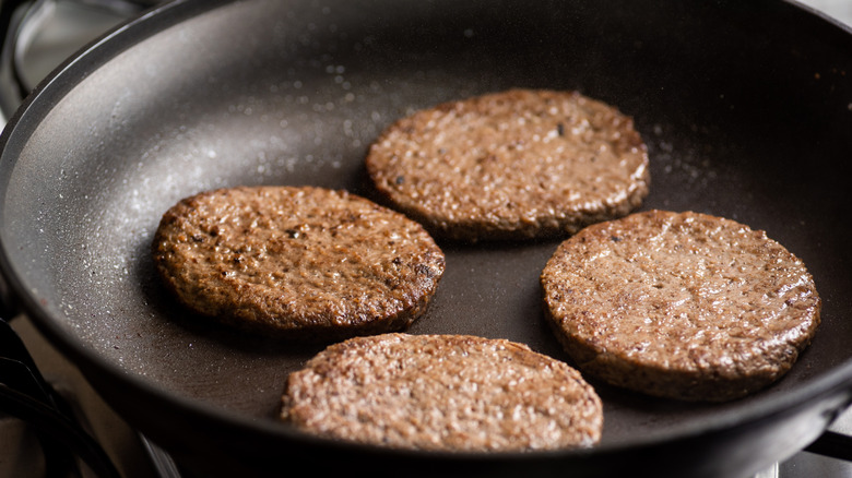 Four hamburger patties cooking in a frying pan