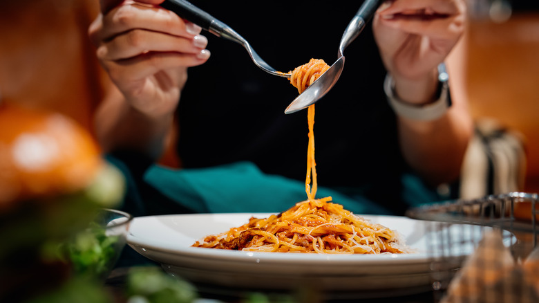Person eating spaghetti with a fork and spoon