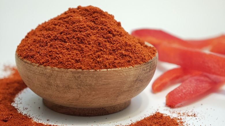Smoked paprika powder in a wooden bowl with red peppers behind it