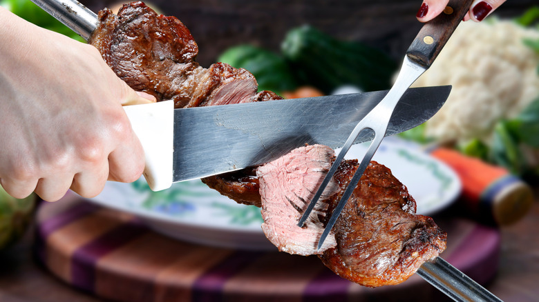 Meat on a skewer being sliced with a knife