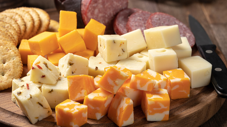 A cutting board with cubes of cheese, crackers, and salami.