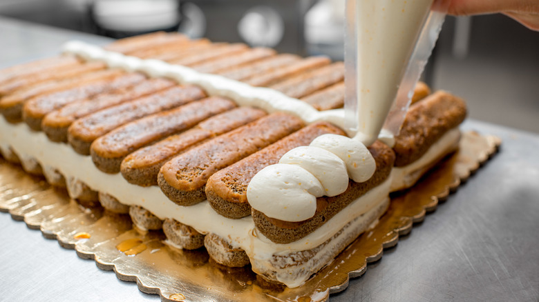 Person piping mascarpone filling on tiramisu