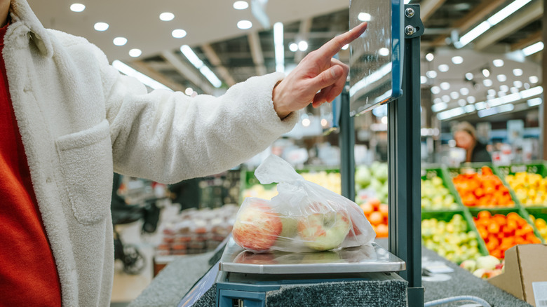A bag of apples on a grocery store scale with a customer tapping a touch screen above it.