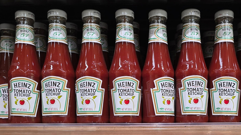 Bottles of Heinz ketchup lined up on a supermarket shelf.