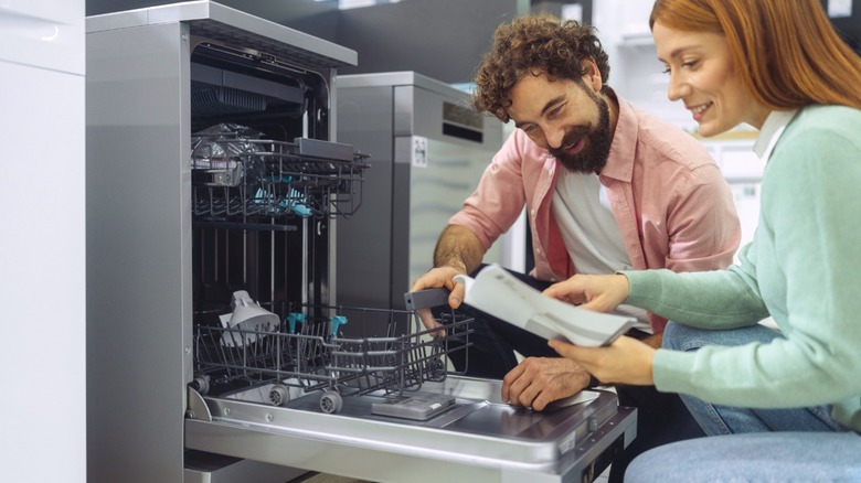Couple reading manual of expensive dishwasher on display in store.